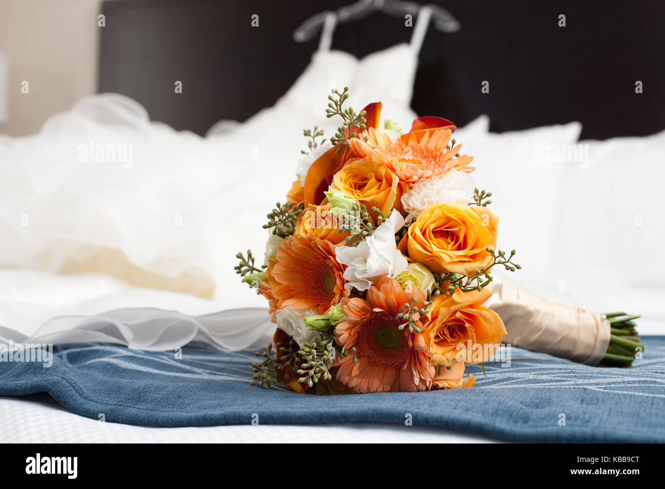 Orange Strauß Blumen auf einem Bett mit Wedding Dress hinter Stockfoto