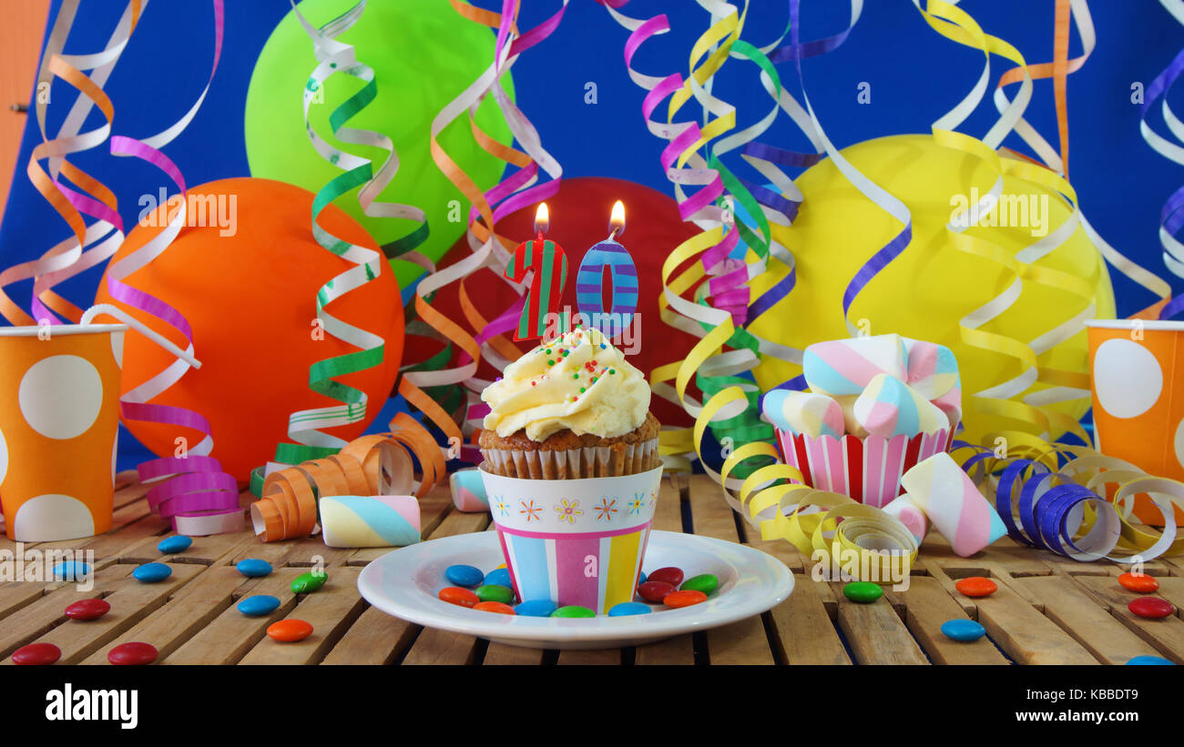 20 Geburtstag Kuchen mit Kerzen brennen auf der rustikalen Holztisch mit Hintergrund von bunten Luftballons plastik becher Bonbons auf der blauen Wand im Hintergrund Stockfoto