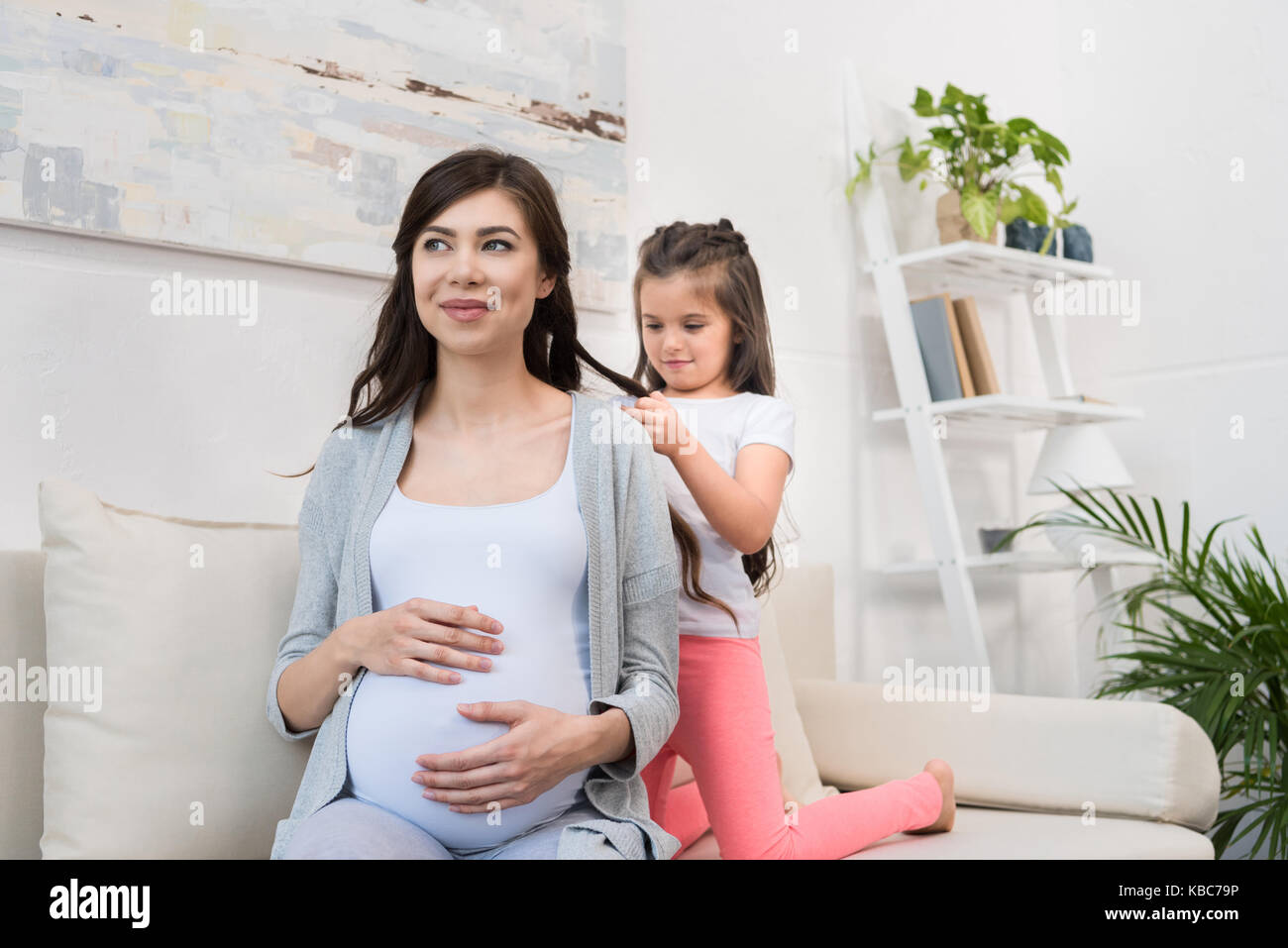 Kleines Mädchen flechten Haar der schwangeren Mutter Stockfoto