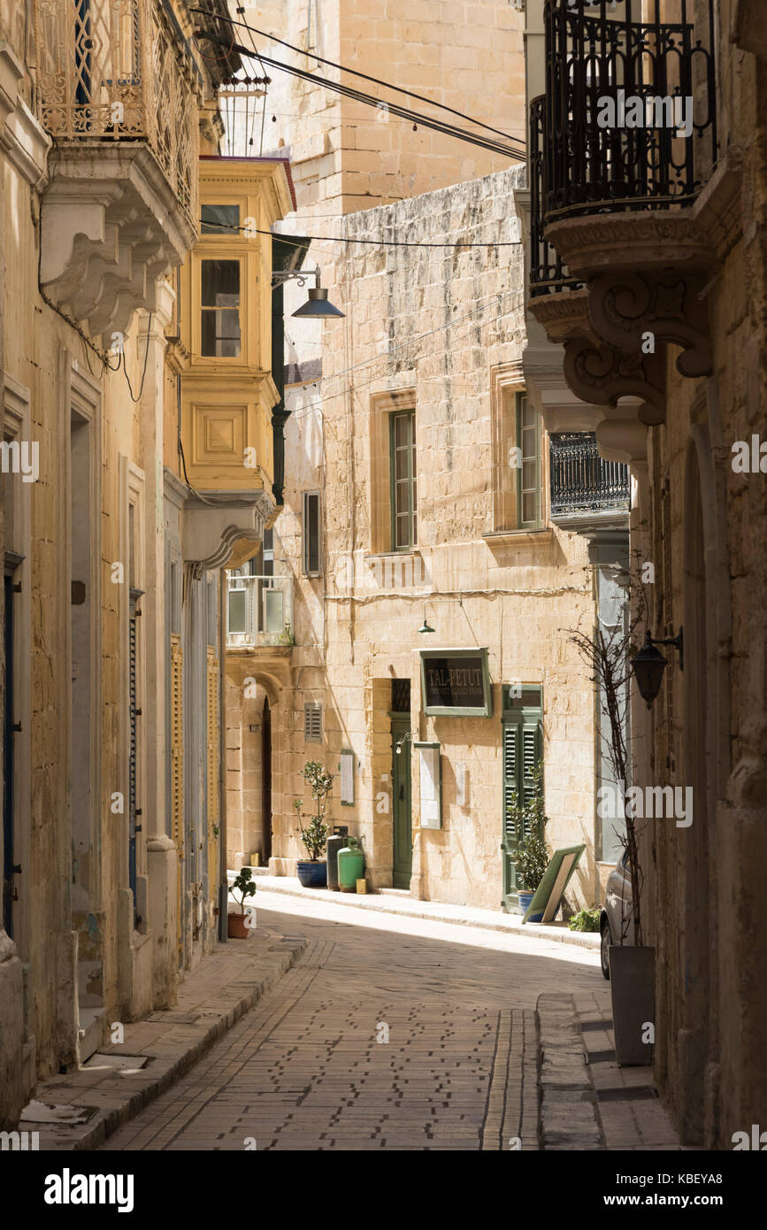 Eine schmale Straße in der mittelalterlichen Stadt von Vittoriosa Malta mit alten honigfarbenen Steingebäude und gepflasterten Pfad Stockfoto
