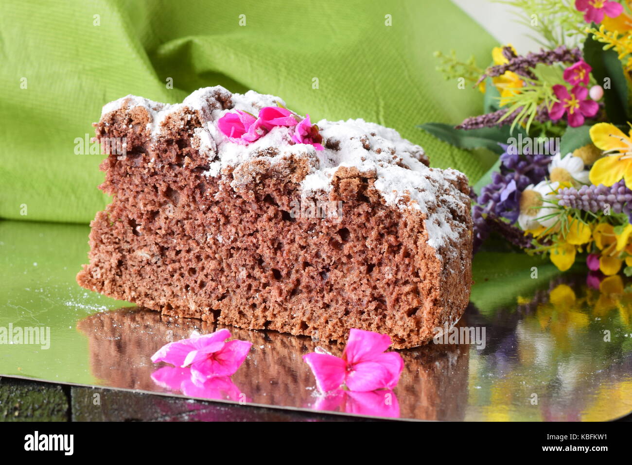 Ein Stück leckere hausgemachte Schokolade Kuchen auf einem silbernen Schild mit Blumen und grünes Tuch als Hintergrund. Home Kochen. Feste, Ferien, Geburt Stockfoto