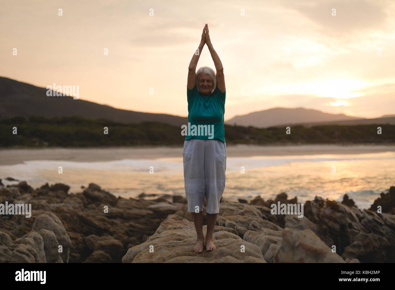 Ältere Frau Yoga am Meer Felsen bei Sonnenuntergang Stockfoto