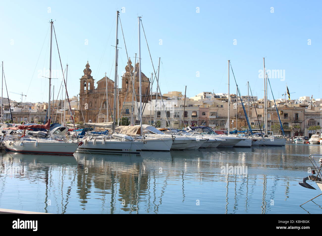 Boote in einem maltesischen Hafen mit einer Kirche im Hintergrund, und starke Reflexionen im Wasser an einem sonnigen Tag, Malta, September 2017 Stockfoto
