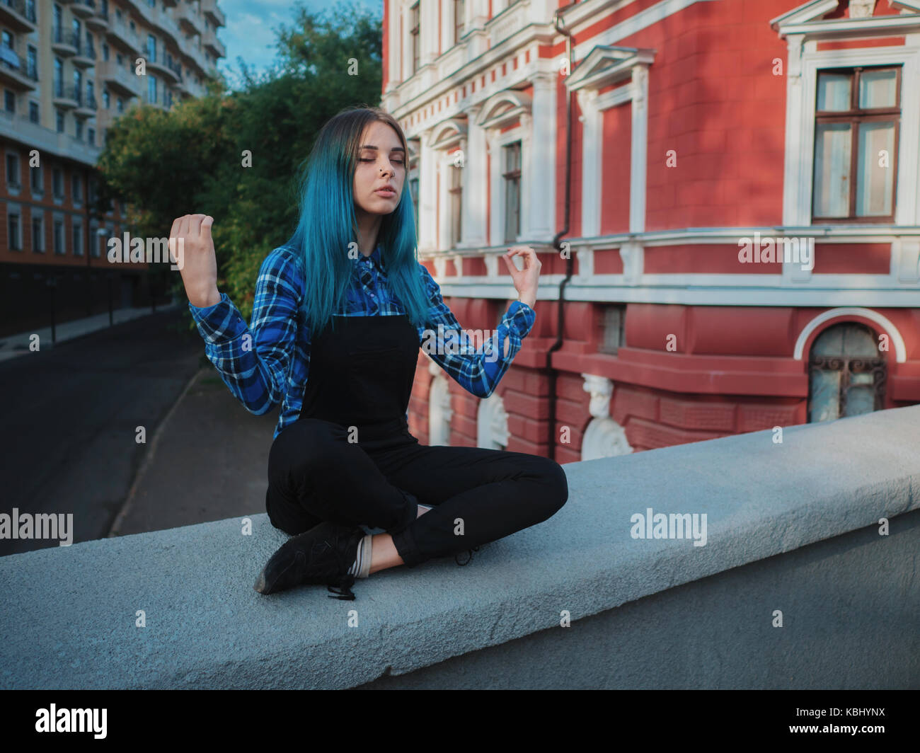 Ruhige Straße Punk oder Hippie Mädchen mit blau gefärbten Haaren. Frau mit Piercing in der Nase, ungewöhnliche Frisur meditieren auf Europäischen leere Straße. Yoga Konzept Stockfoto