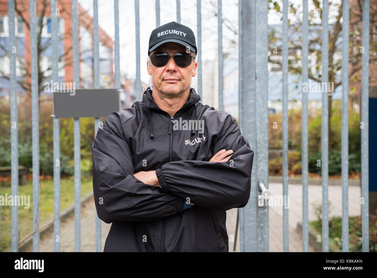 Portrait von zuversichtlich ausgereifte Security Guard stand mit verschränkten Armen vor Tor Stockfoto