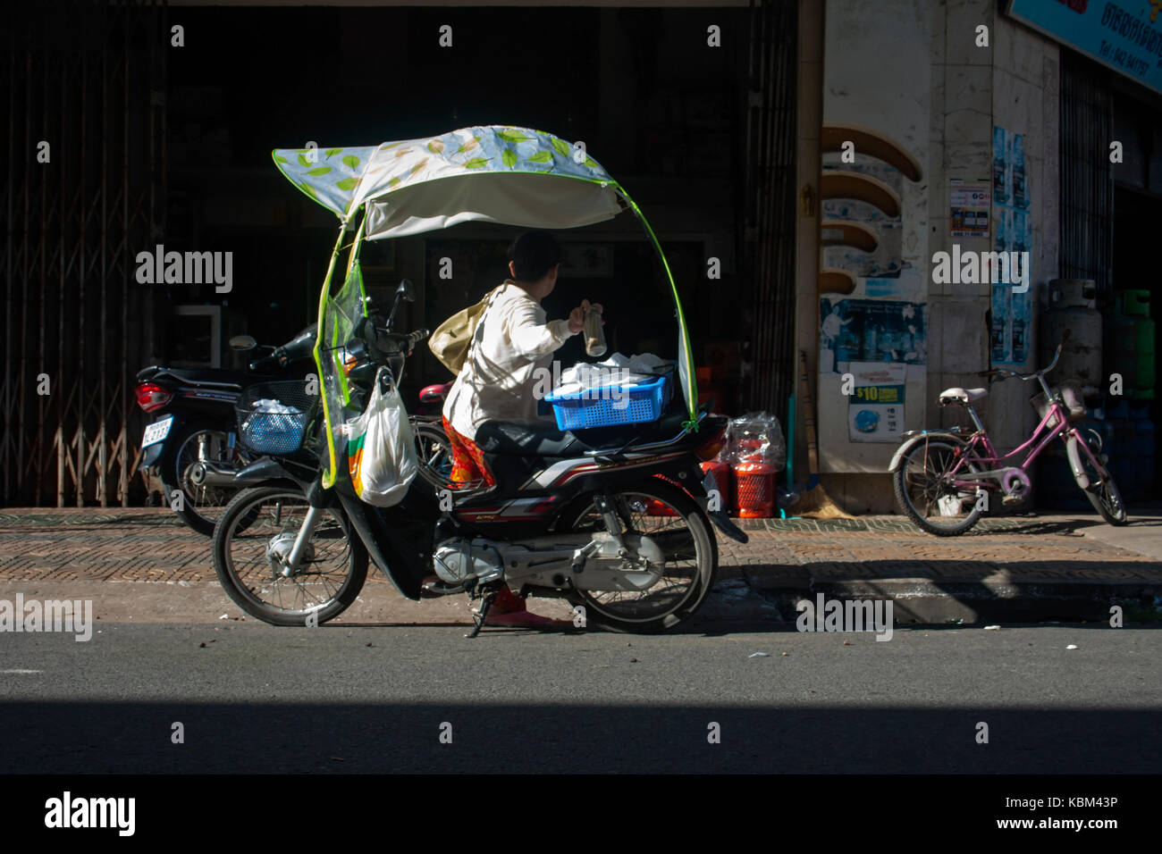 Ein Lebensmittel ist der Verkäufer Lieferung von Nahrung mit einem Motorrad mit einem Vordach, wie sie ihre Runden macht in Kampong Cham, Kambodscha. Stockfoto