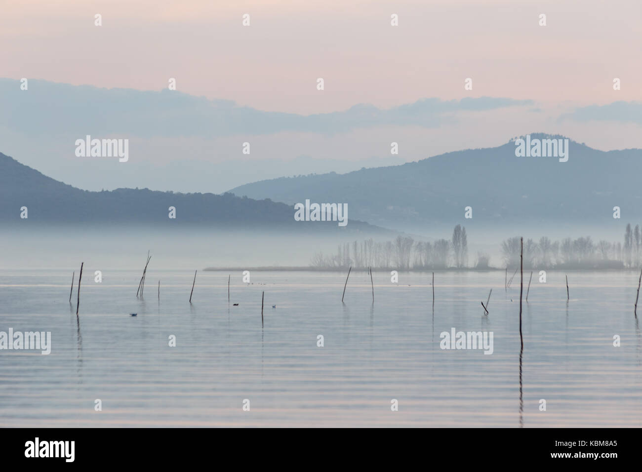 See in der Dämmerung, bei Nebel und schöne, weiche und warme Farben und Holzpfähle im Vordergrund. Stockfoto