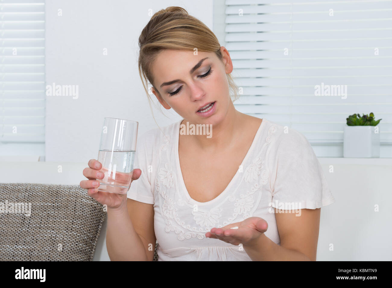 Junge Frau mit Tabletten und Wasser Glas beim Sitzen auf dem Sofa zu Hause Stockfoto