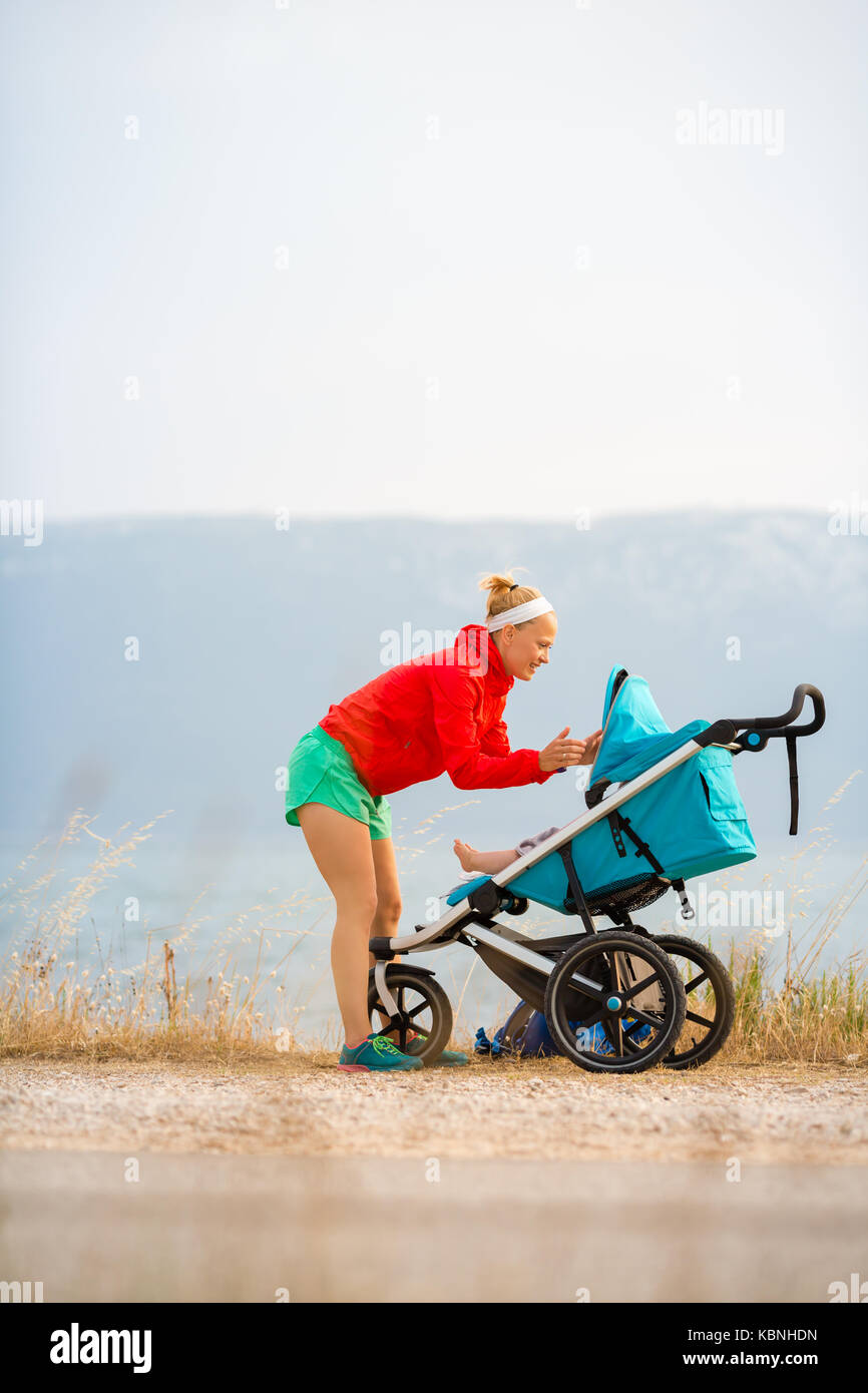 Mutter mit Kind im Kinderwagen bei Mutterschaft bei Sonnenuntergang und Bergwelt. Joggen oder Walken Frau mit Kinderwagen bei Sonnenuntergang. Schön ins Stockfoto