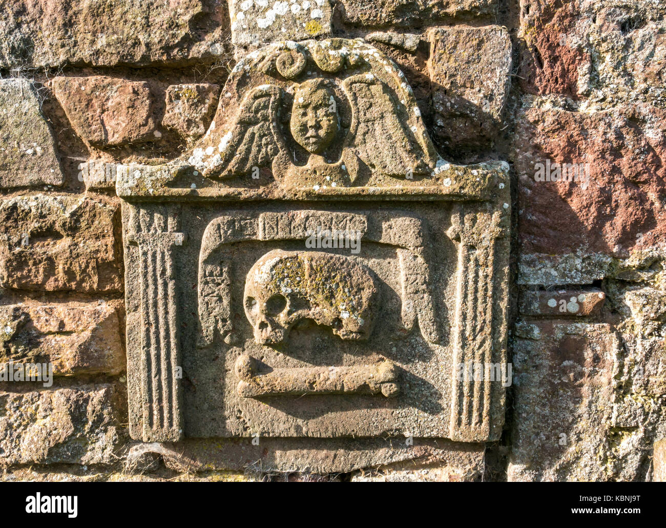 Nahaufnahme eines abgenutzten Grabsteins mit Totenkopf und Kreuzknochen und Engel auf dem Dorffriedhof von Stenton, East Lothian, Schottland, Großbritannien Stockfoto