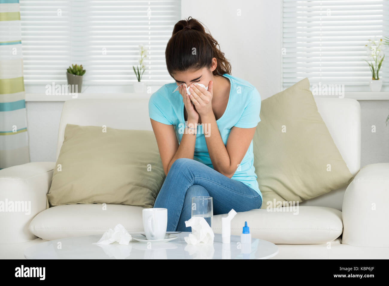 Kranke junge Frau blasen Nase, während auf dem Sofa zu Hause sitzen Stockfoto