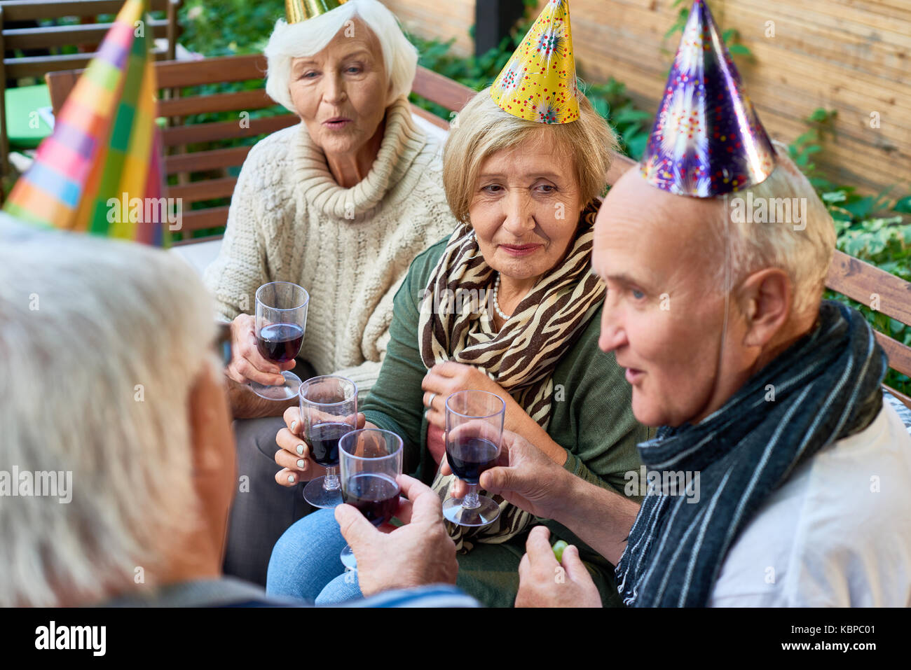 Gruppe der älteren Freunde tragen warme Kleidung, Brille mit roten Jammern in den Händen und plaudern miteinander, während mit Outdoor Party Stockfoto