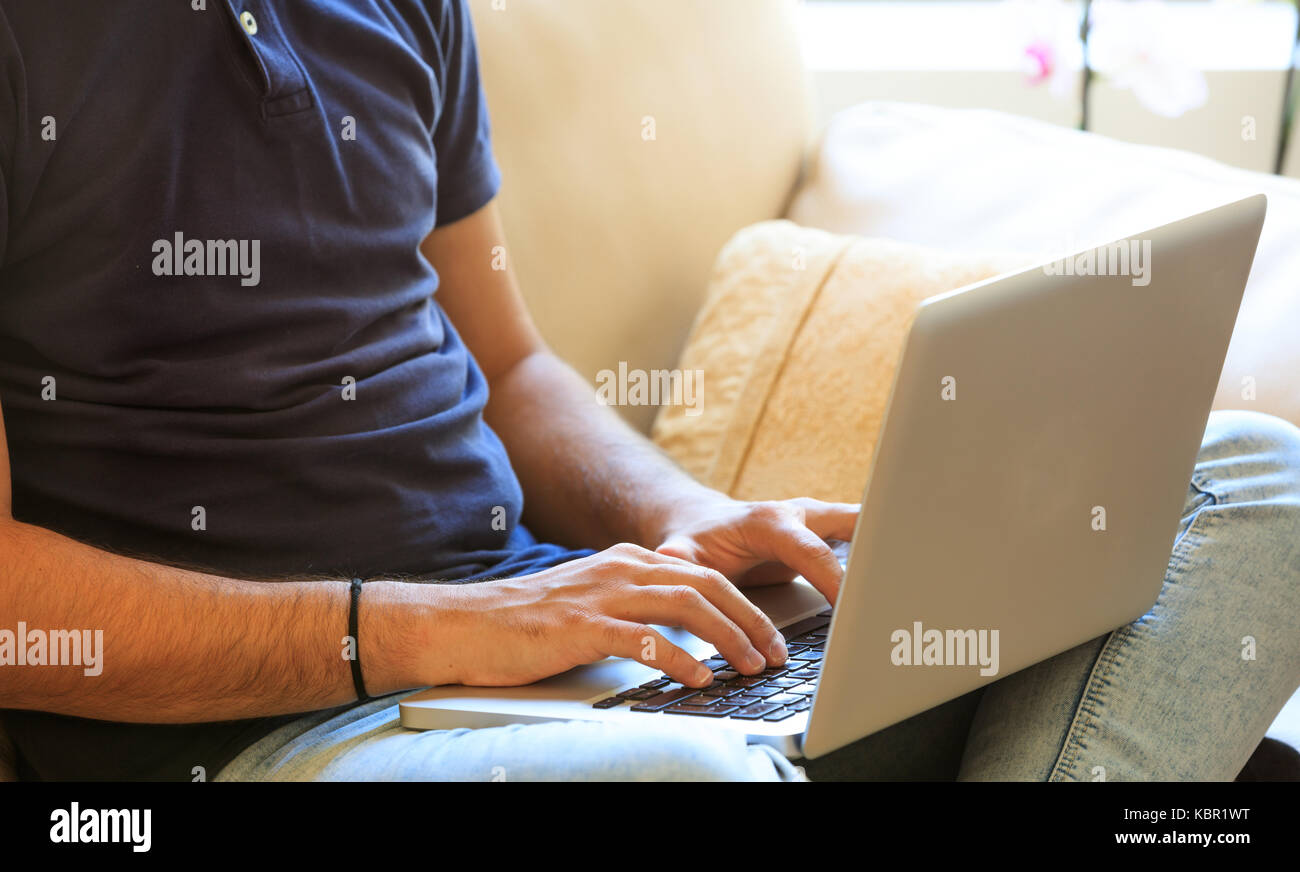 Junger Mann mit einem Laptop auf dem Sofa zu Hause sitzen arbeiten Stockfoto