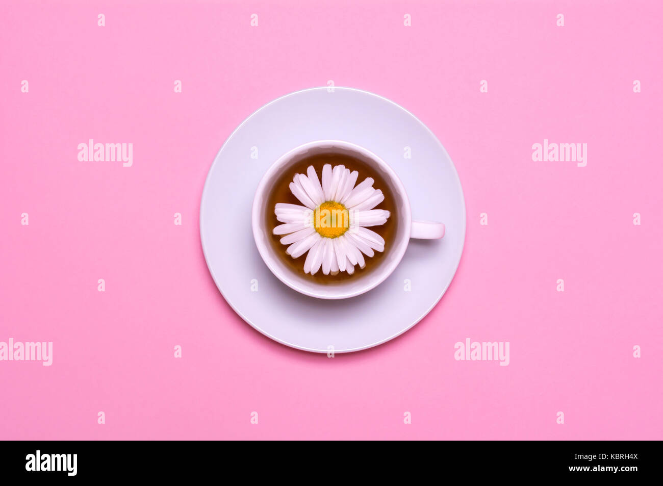 Weiße Tasse mit Kamillentee auf einem rosa Hintergrund. Blick von oben. Kreative Gestaltung. Stockfoto