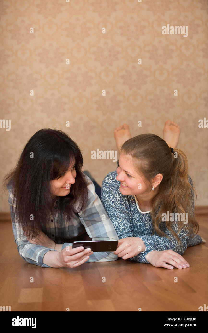 Zwei junge hübsche Frauen auf dem Boden liegend Holding smart phone Stockfoto