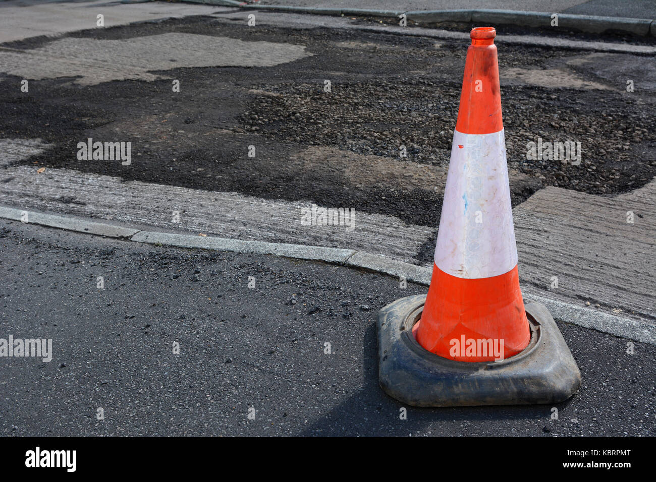 Hell orange und weiß Leitkegel auf einem Gehsteig, beschädigte Fahrbahn jenseits, bei Reparaturarbeiten an den Asphalt Stockfoto