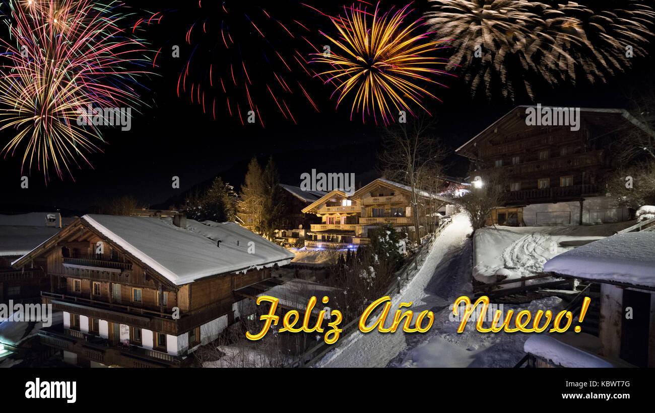 Vorabend des neuen Jahres mit alpinen Dorf im Schnee, Feuerwerk, Text "Feliz Ano Nuevo!' Stockfoto