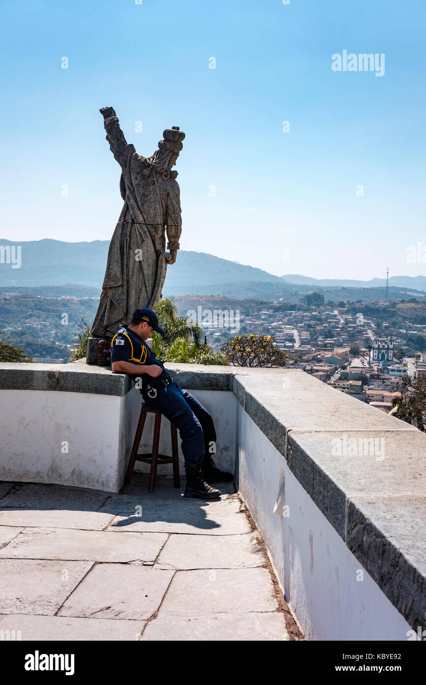 Männliche Municipal Guard officer Kontrolle sein Handy neben dem Speckstein Statue der Prophet Habakuk, die von Aleijadinho, Congonhas, Minas Gerais, Brasilien. Stockfoto