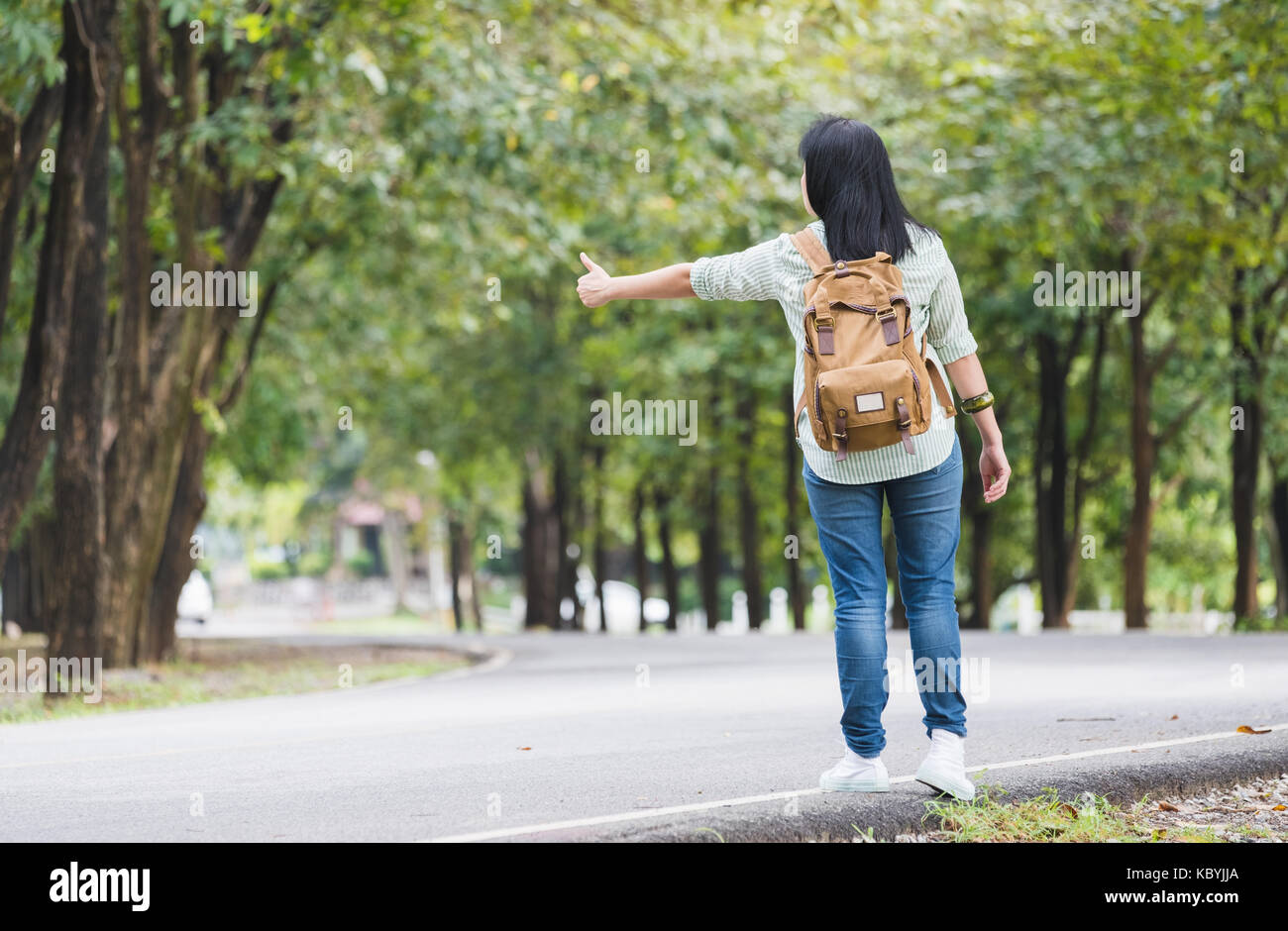 Asiatische Frau Backpacker auf Landstraße mit Baum im Frühjahr saisonale, allein reisen oder Alleinreisende Konzept. Stockfoto