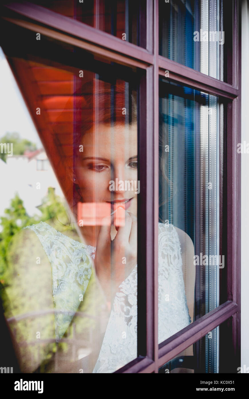 Junge attraktive dunkle Haare Dame suchen durch ein Fenster. Vertikale Nahaufnahme Porträt. Junge Frau auf der Suche nach einem Fenster mit Fenster Glas als Spiegel Stockfoto