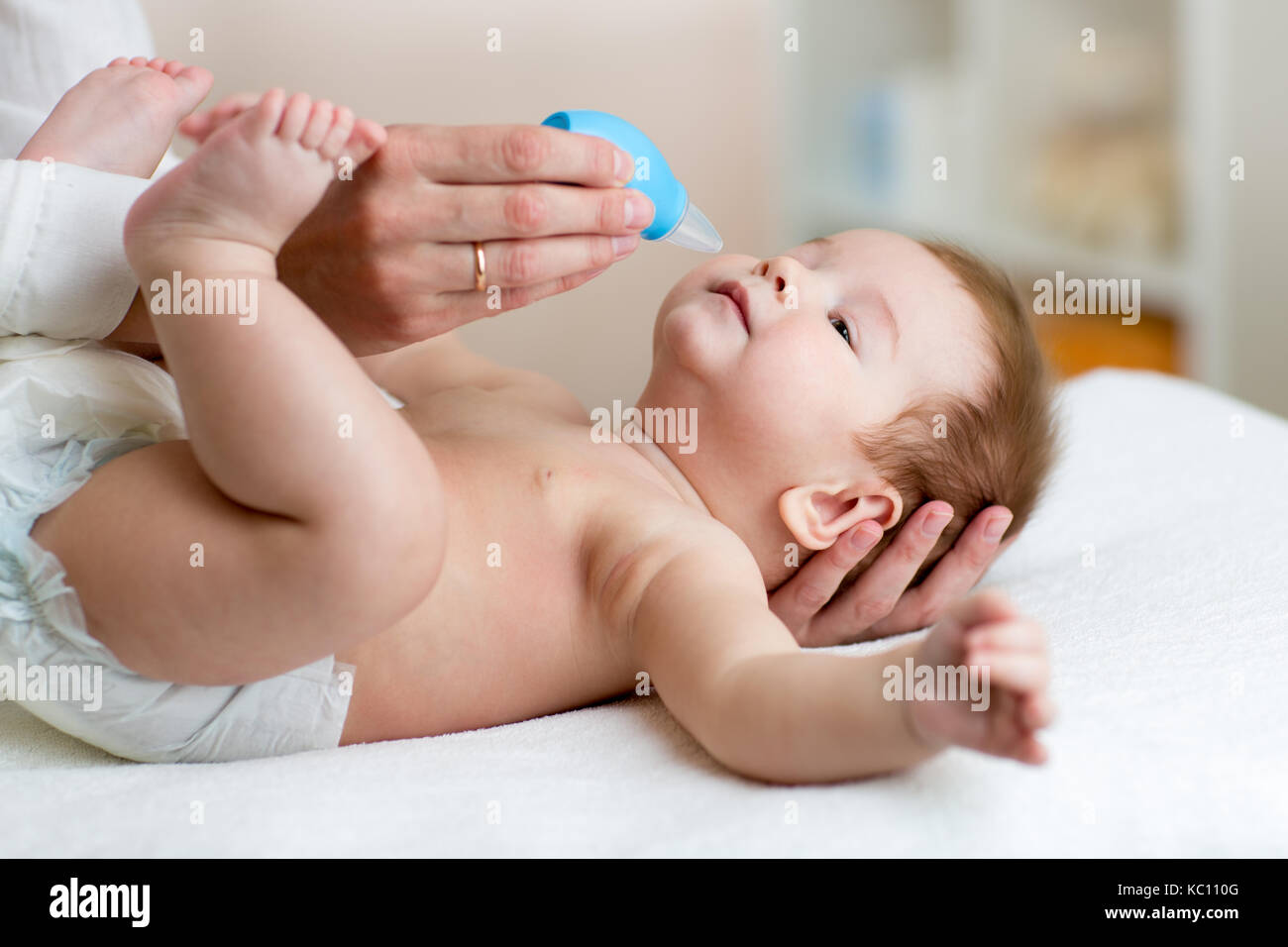 Mutter oder Arzt reinigt Babys Nase mit Gebläse, während Kind tot liegt und lächelnd. Stockfoto