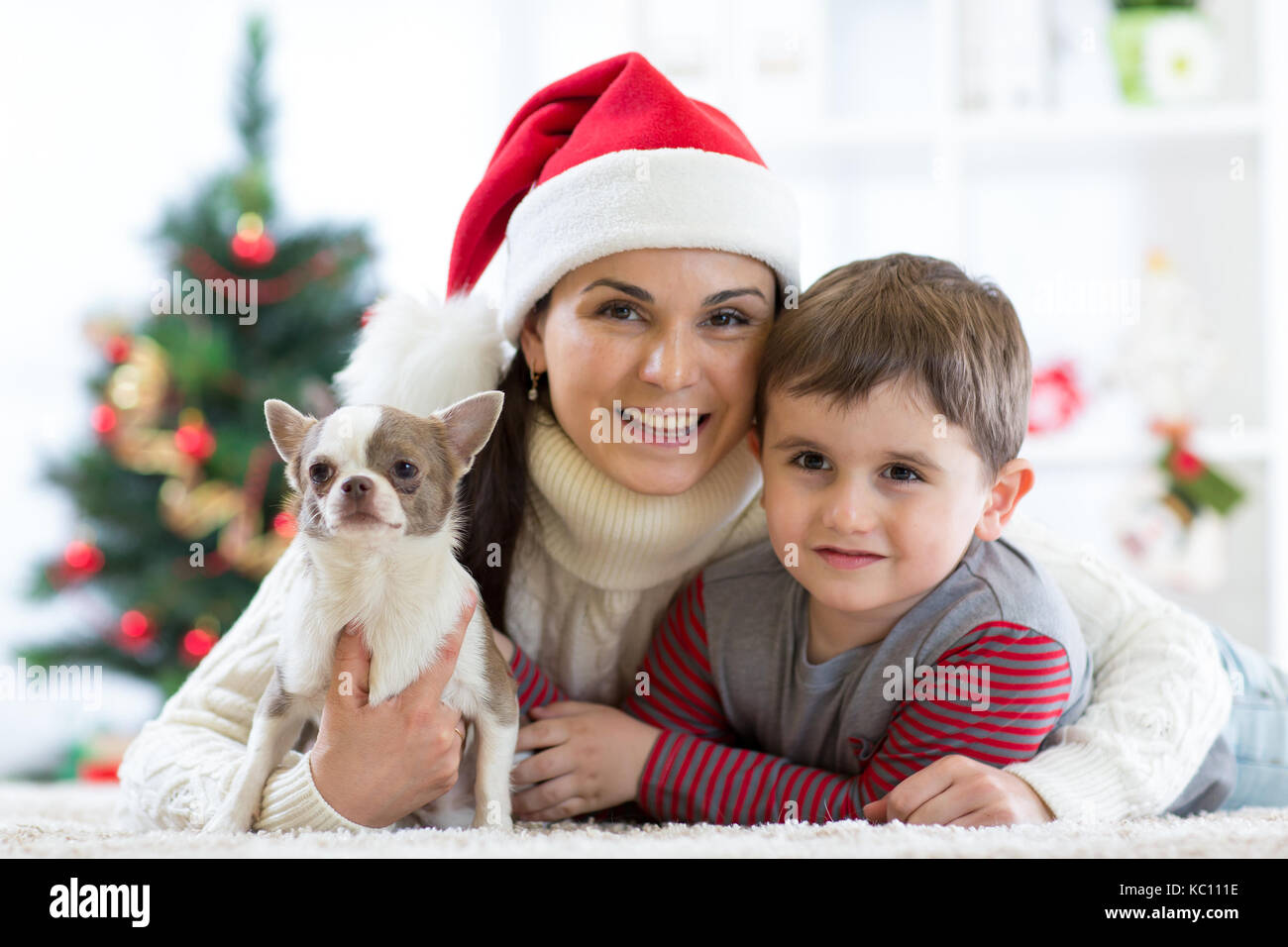 Frau und Sohn Weihnachten feiern mit pelzigen Freund. Mutter und Kind mit Terrier Hund. Hübsches Kind Junge mit Hund an x-mas Tree. Stockfoto