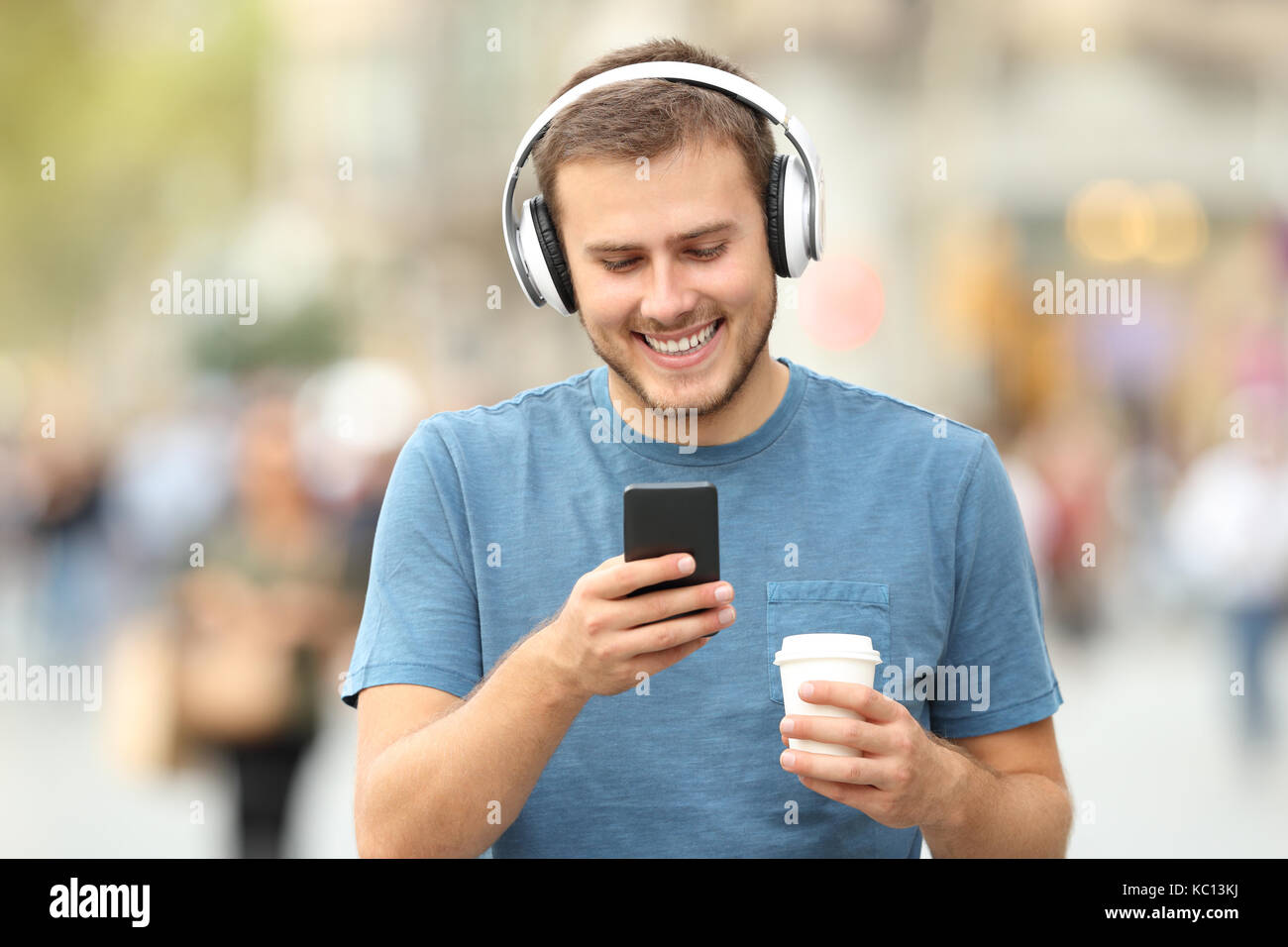 Vorderansicht eines glücklichen Mann, Musik hören mit Kopfhörern und halten ein Drink auf der Straße Stockfoto