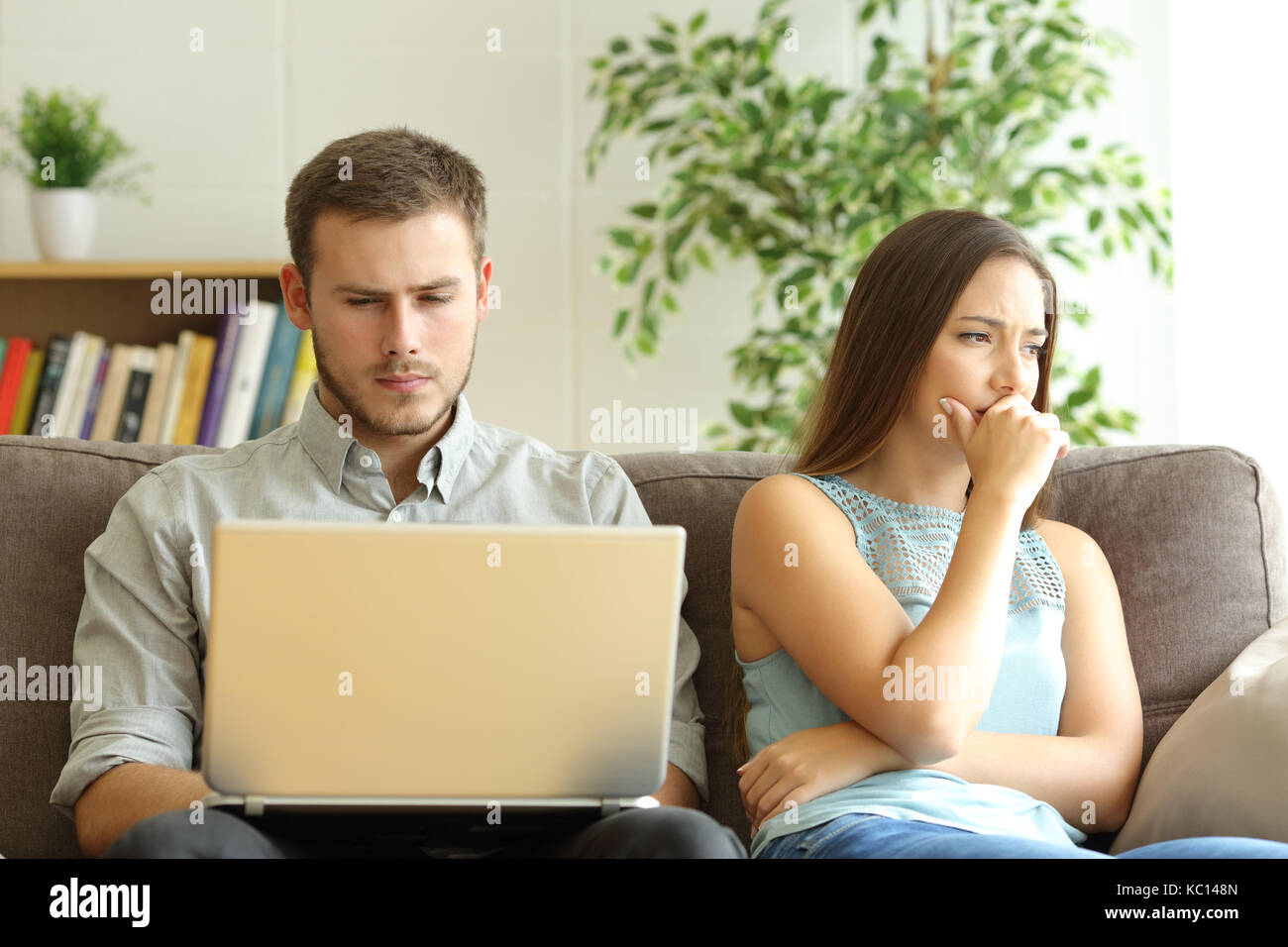 Mann mit Laptop auf Linie zu seiner traurigen Frau auf einem Sofa zu Hause sitzen ignorieren Stockfoto