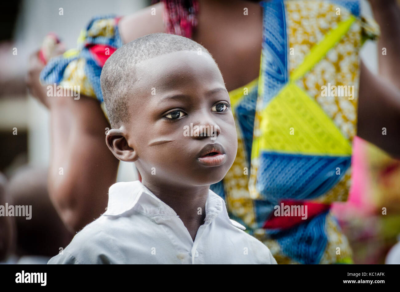 Portrait von afrikanischen Jungen mit traditionellen Gesichts Narben und bunte Frau im Hintergrund, matadi, Kongo, Afrika Stockfoto