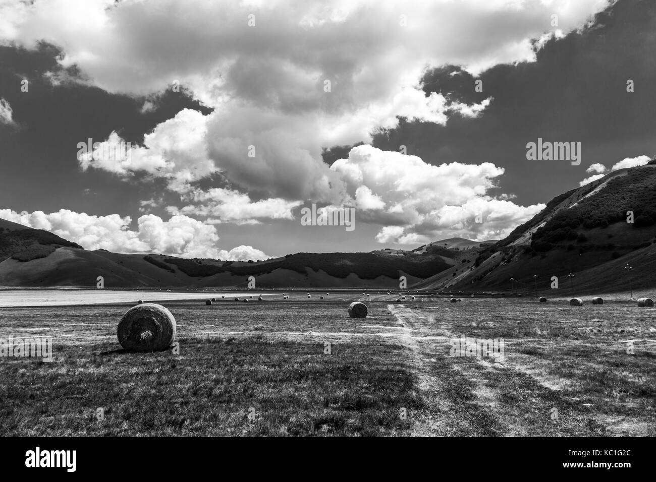Einige Strohballen auf castelluccio Di Norcia (Umbrien) bewirtschafteten Feldern, mit tiefen Himmel und weißen Wolken Stockfoto