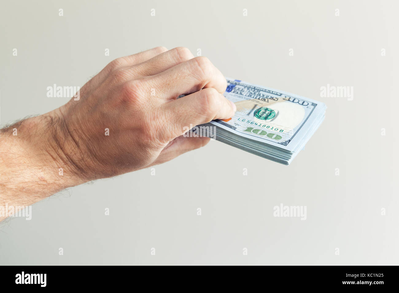 Bündel von einhundert Dollar Noten in der Hand über die weiße Wand im Hintergrund Stockfoto