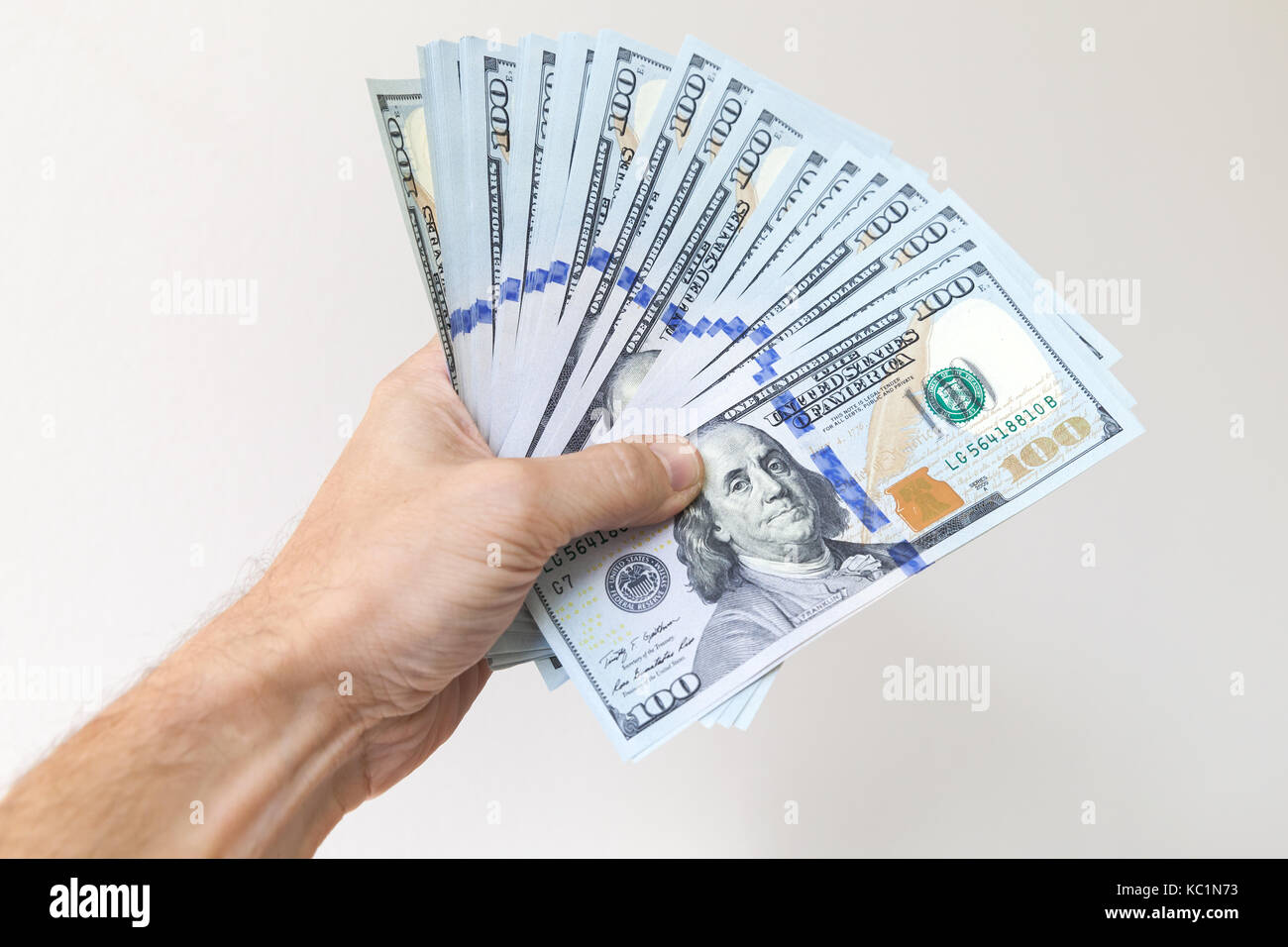 Fan von einhundert Dollar Noten in männlicher Hand über weiße Wand im Hintergrund Stockfoto