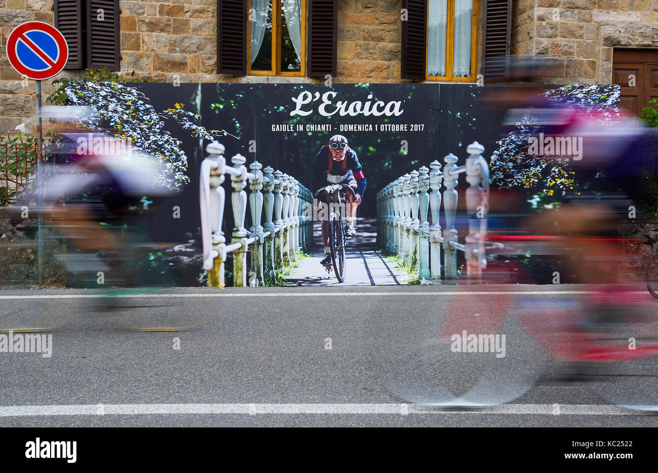 Toskana, Italien. 1. Okt 2017. Radfahrer fahren die Oldtimer, vorbei an einem Plakat im Gedächtnis von Luciano Berruti, die 20 Mal der insgesamt 21 Ausgaben verbunden hat, während der 'Eroica' Radfahren Veranstaltung für alte Fahrräder im Chianti Gebiet in der Toskana, Italien, am Okt. 1, 2017. Mehr als 7.000 Radfahrer, tragen Vintage cycling Jerseys, Reiten Fahrräder Jahrgang 1987 oder früher teilgenommen, in der "Eroica" (heroisch) Radfahren Veranstaltung durch die Strade Bianche, die schotterpisten von Chianti in der Toskana. Credit: Jin Yu/Xinhua/Alamy leben Nachrichten Stockfoto