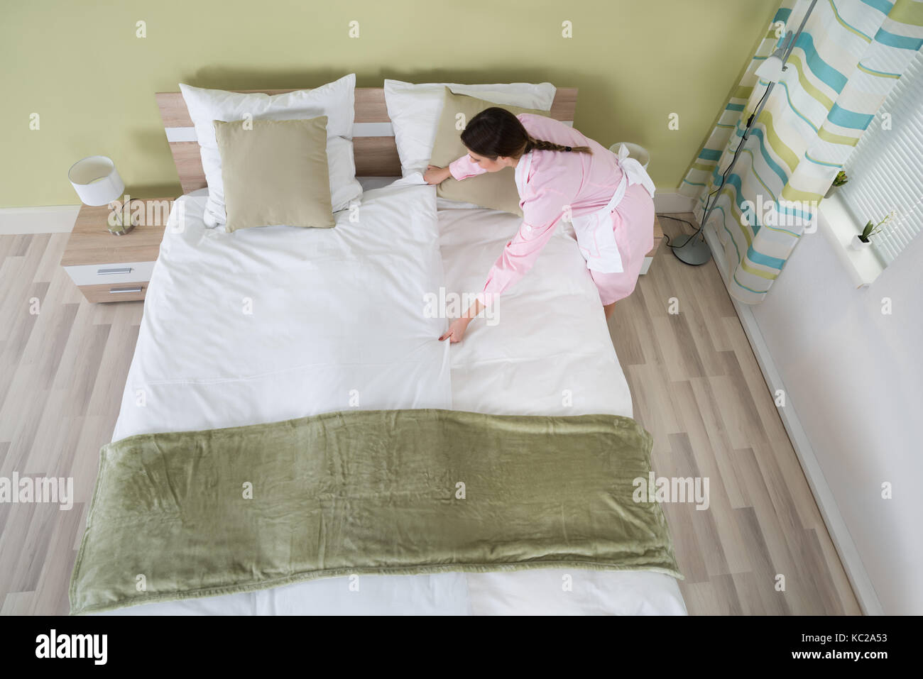 Junge weibliche Haushälterin, die die Bettlaken auf dem Bett im Zimmer Stockfoto