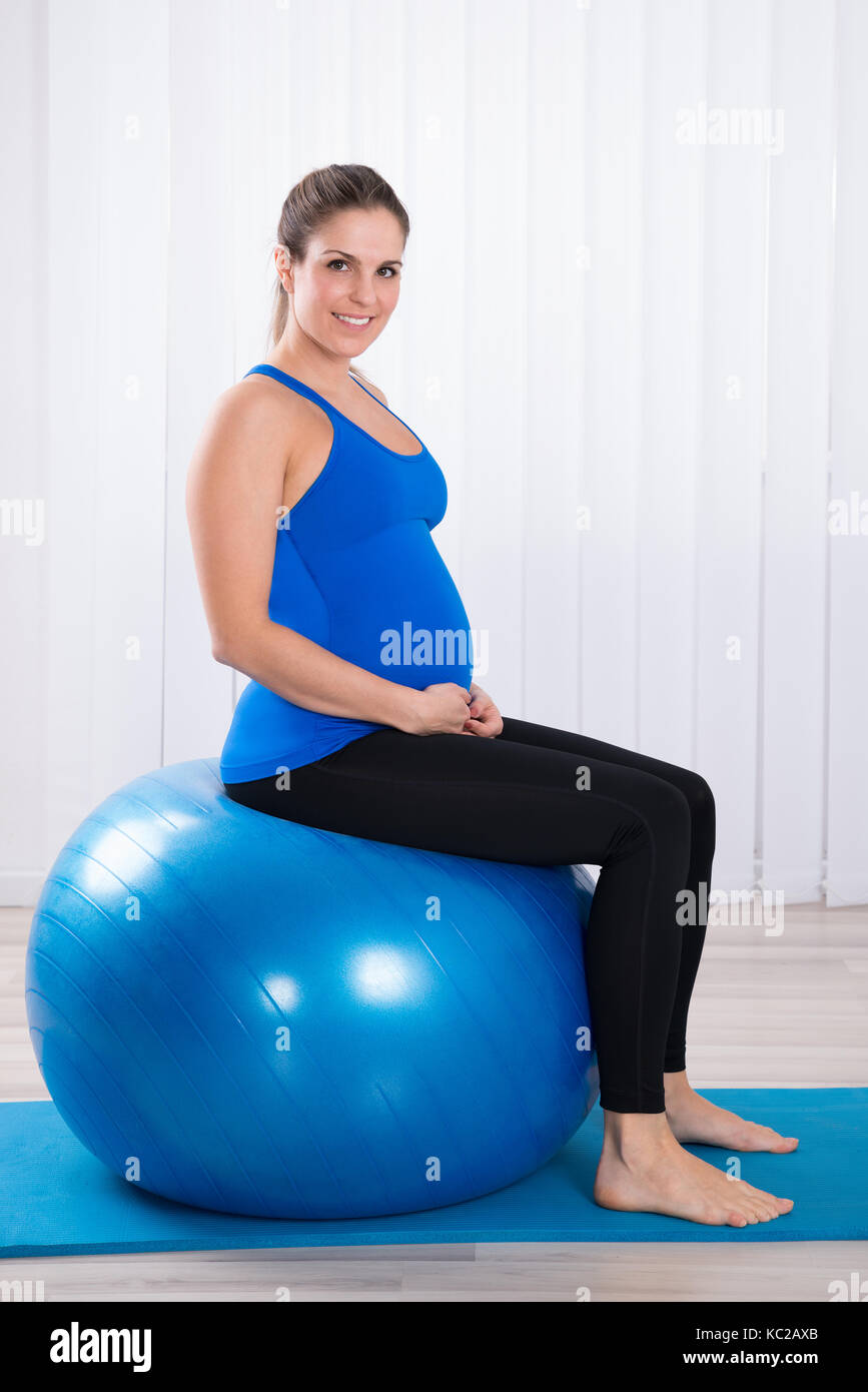 Glückliche junge Frau auf Fitness Ball zu Hause sitzen Stockfoto
