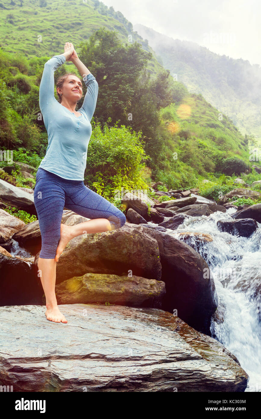 Frau in Yoga Asana Vrikshasana Baum am Wasserfall im Freien Stockfoto