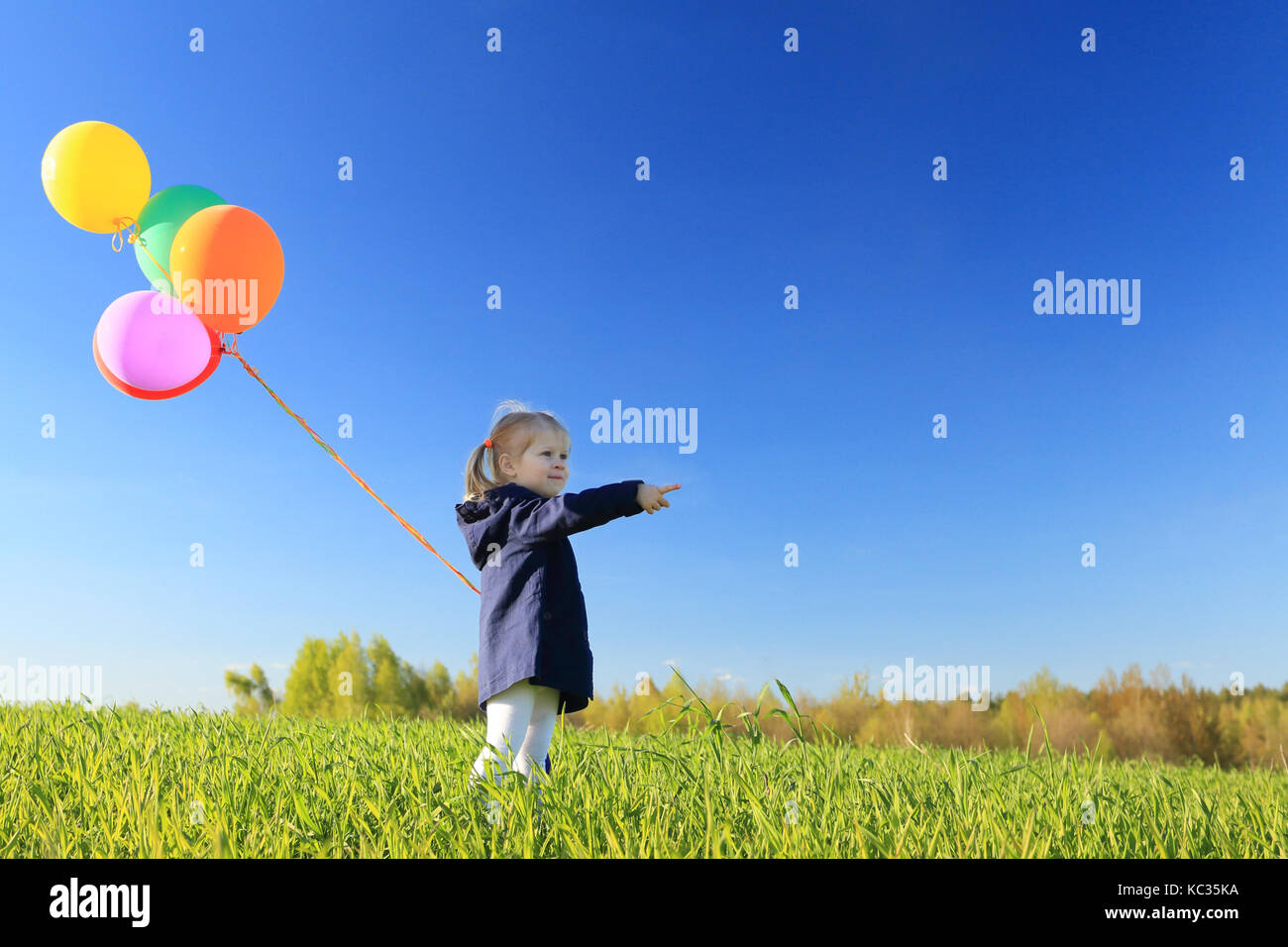 Glückliche kleine Mädchen mit Ballons auf der grünen Wiese. Mädchen mit bunten Luftballons Punkt vor. Kind glück Konzept. Stockfoto