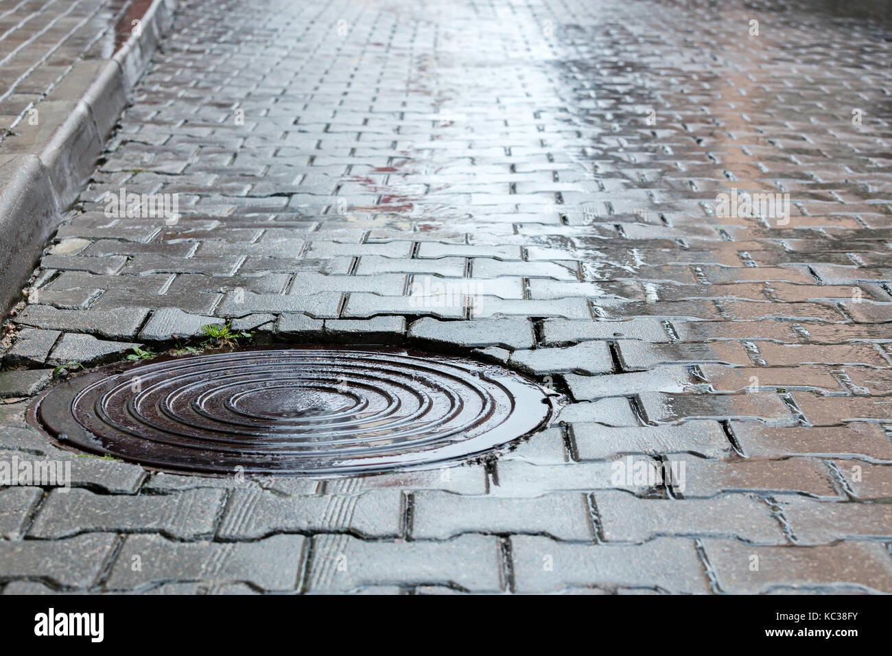 Rundstahl Abwasserkanal Mannloch auf dunklen nassen Kopfsteinpflaster Straße Stockfoto