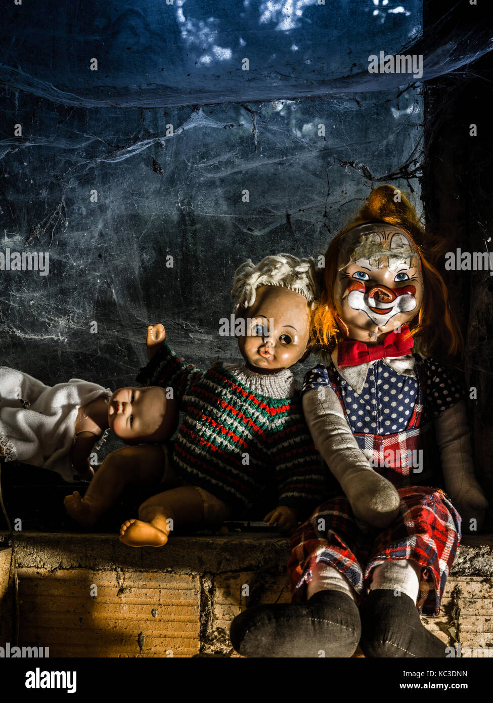 Foto von alten Puppen und eine Axt ruht auf einem alten Fensterbank in Spinnweben und Staub bedeckt. Stockfoto