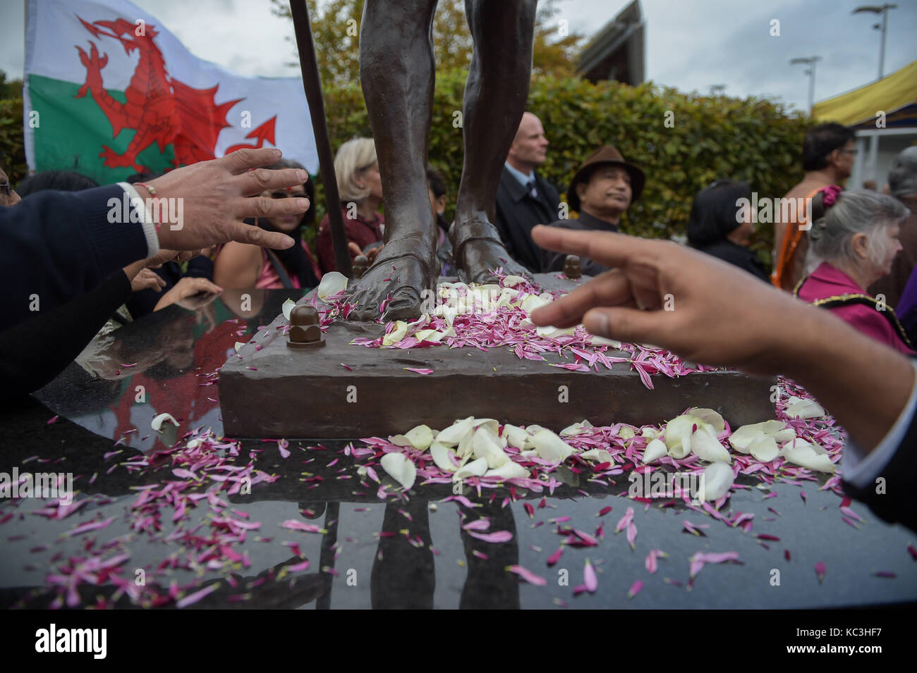 Menschen verbreitet Blütenblätter zu Füßen der Statue von Mahatma Gandhi, wie es in der Bucht von Cardiff, Wales vorgestellt, der Tag seiner Geburt im Jahre 1869 zu markieren und den Internationalen Tag der Gewaltlosigkeit, die auch am 2. Oktober gefeiert wird. Stockfoto