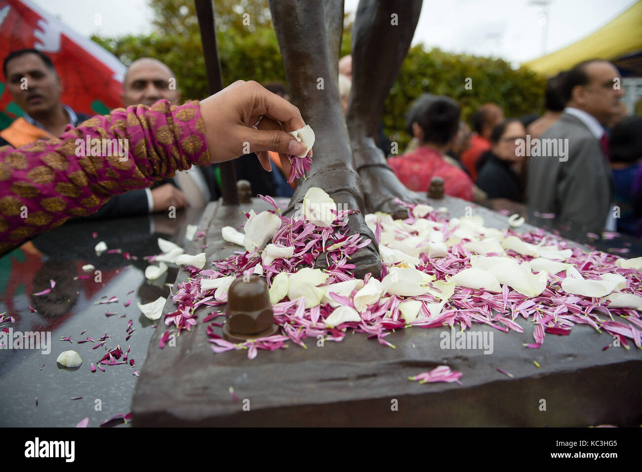 Menschen verbreitet Blütenblätter zu Füßen der Statue von Mahatma Gandhi, wie es in der Bucht von Cardiff, Wales vorgestellt, der Tag seiner Geburt im Jahre 1869 zu markieren und den Internationalen Tag der Gewaltlosigkeit, die auch am 2. Oktober gefeiert wird. Stockfoto