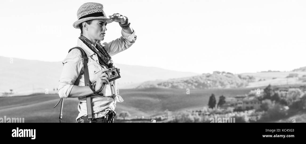 Entdecken Sie magische Ausblicke der Toskana. junge Frau Wanderer in Hut mit Tasche wandern in der Toskana mit Vintage Foto Kamera in die Ferne suchen Stockfoto