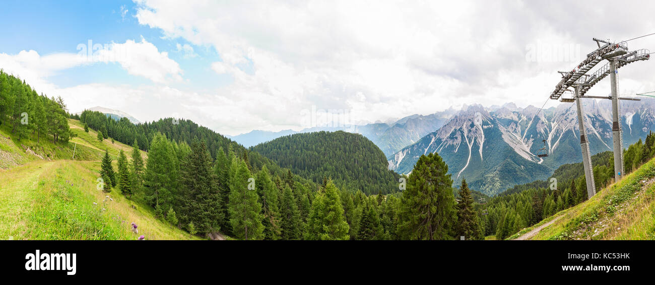 Bergpanorama mit Wald, Dolomiten, das Tal und die Sesselbahn im Sommer. Himmel mit Wolken. Stockfoto