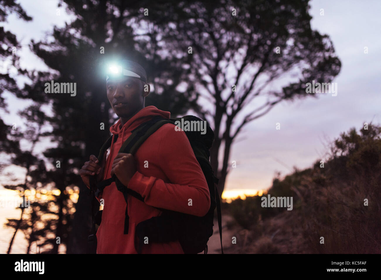 Junge afrikanische Mann mit einem Scheinwerfer wandern in der Dämmerung konzentriert Stockfoto