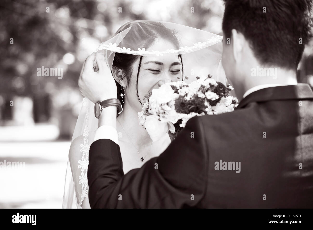 Asiatische Bräutigam anheben Bridal Veil schöne Braut, Schwarz und Weiß zu küssen. Stockfoto