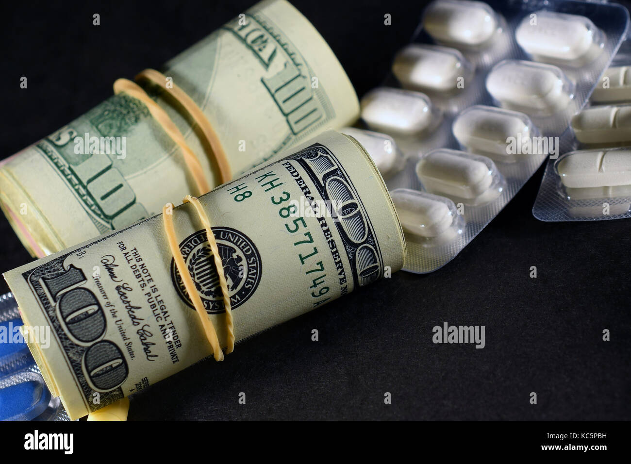 Rollen mit Geld, us-Dollar und verschreibungspflichtigen Medikamenten auf dunklem Untergrund. Stockfoto