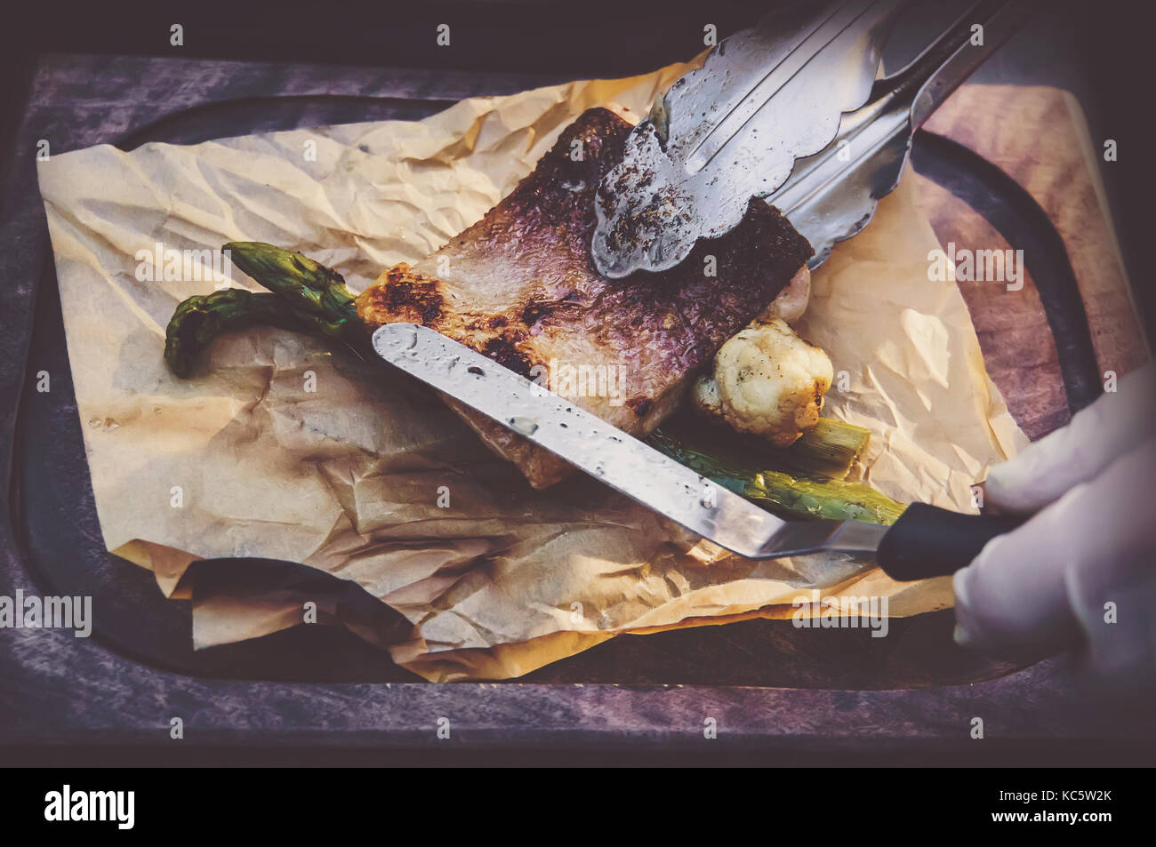 Prozess der Küche Fisch. Hände Köche in saubere, weiße Handschuhe setzt gegrillten Fisch auf dem Papier liegen auf dem Board. Stockfoto