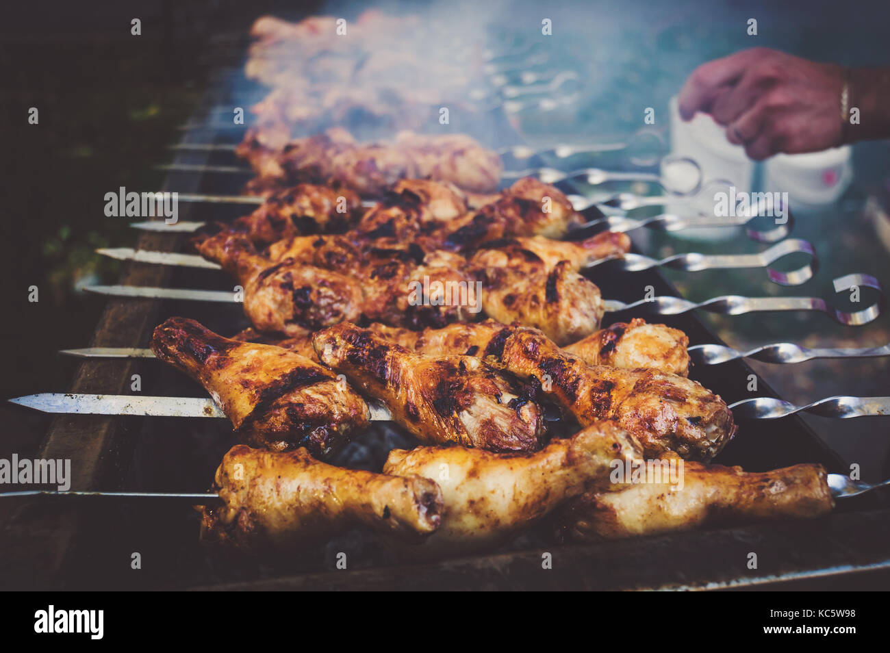 Koch hält ein Spieß mit gegrilltem Huhn in seiner Hand. gebratene Hähnchenschenkel auf dem Grill Stockfoto