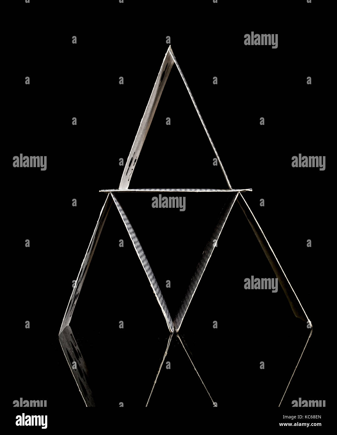 Haus der Karten aus weißem Spielkarten, frontal geschossen, die auf einem klaren reflektierende Glasoberfläche, schwarzer Hintergrund Stockfoto