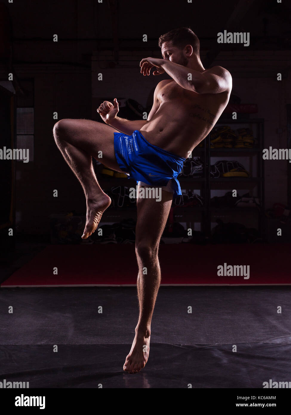 Ein männlicher MMA Fighter Training Kicks und Schläge in einer dunklen Fitnessraum Stockfoto